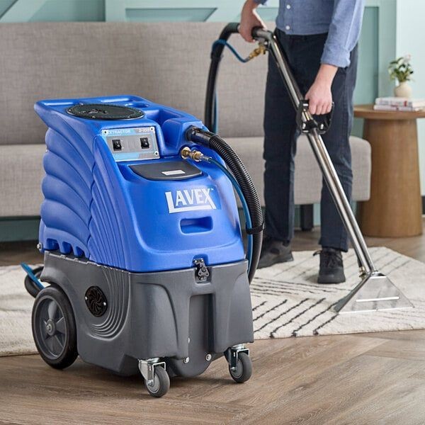 Person using a blue carpet cleaning machine to clean a rug in a living room.