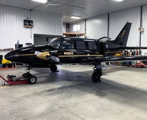 Black private plane parked inside a hangar with gray walls and visible equipment in the background.